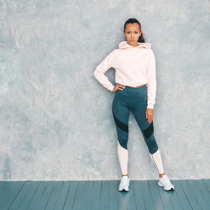 Portrait of fitness woman in sports clothing looking confident.Young female wearing sportswear. Beautiful model with perfect tanned body.Female posing in studio near gray wall